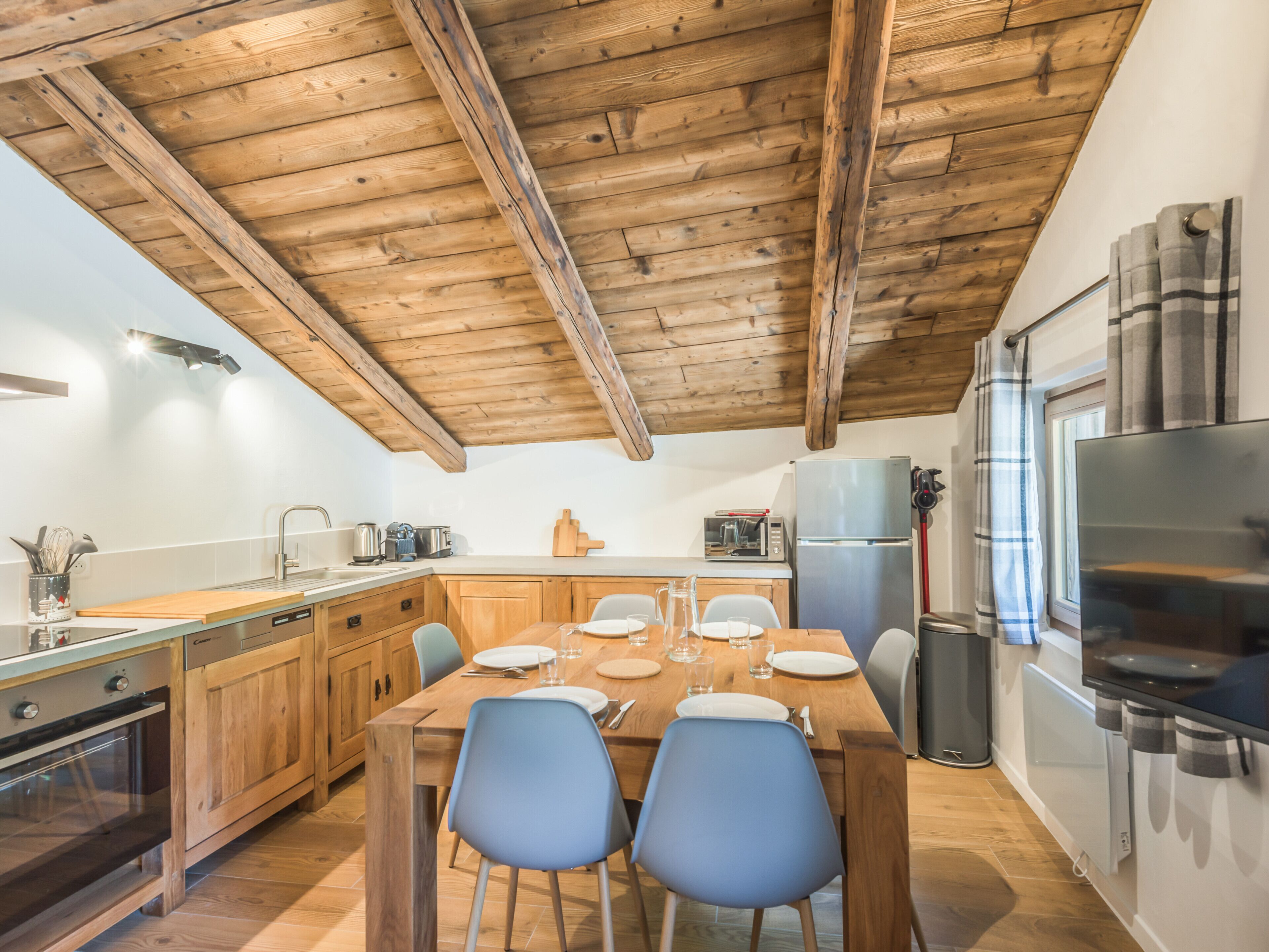Una cucina moderna con travi in legno, elettrodomestici in acciaio inossidabile e un'area pranzo con sedie blu.