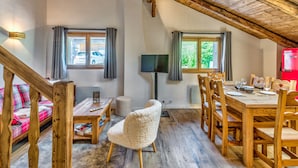 A cozy room with a wooden ceiling, a dining table set with chairs, a sofa, and a television. - Appartement Alpage - Welkeys (Combloux)