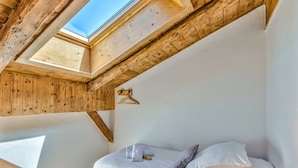 A bedroom with a skylight, wooden beams, a bed with pillows, and a bedside table. - Appartement Alpage - Welkeys (Combloux)