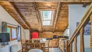 A rustic kitchen with wooden beams, a dining area with chairs, a red refrigerator, and a television on the wall. - Appartement Alpage - Welkeys (Combloux)