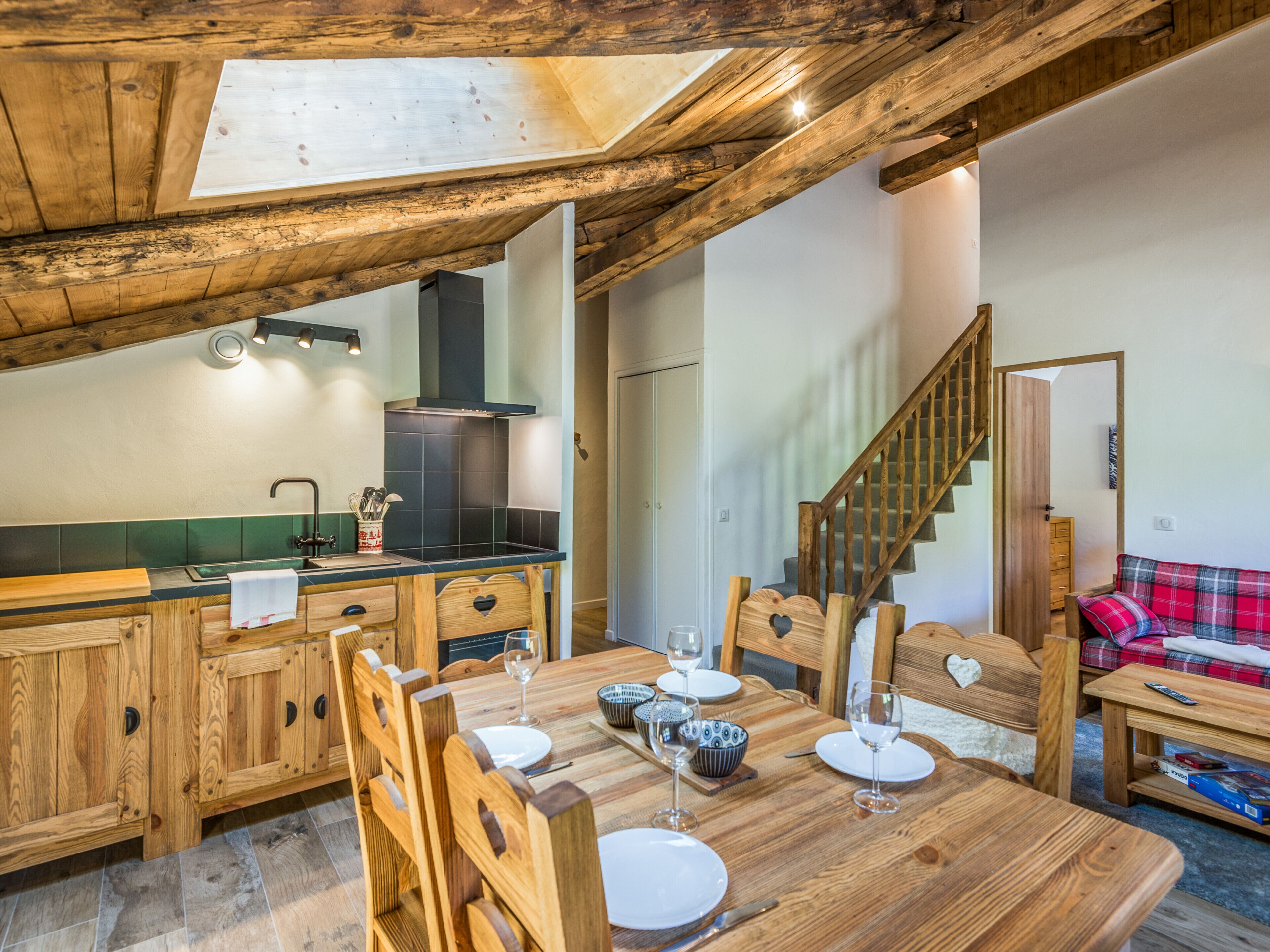 Un coin repas rustique en bois, avec un plafond haut, une cuisine dotée d’un poêle noir et un escalier menant à une autre pièce.