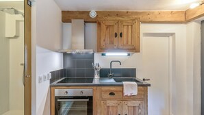 A compact kitchen with wooden cabinets, a built-in oven, a sink, and a modern light fixture.