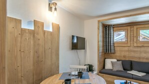 A cozy room with a wooden table, a sofa, and a TV mounted on the wall.