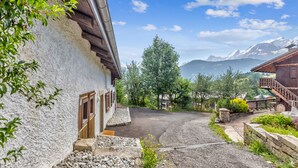 A rustic building with a stone facade, a wooden door, and a gravel driveway leading to a mountain view.