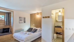 A bedroom with a bed, a wooden wall panel, a painting, a window with curtains, and a bathroom with a mirror and sink.