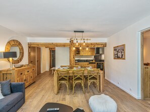 Une cuisine moderne avec des meubles en bois, un coin repas avec une table et des chaises en bois, et un salon avec un canapé et une télécommande sur une table basse.
