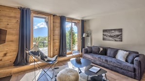 Un salon moderne avec un plancher en bois, un canapé gris, une table basse noire et un fauteuil à motifs noir et blanc.