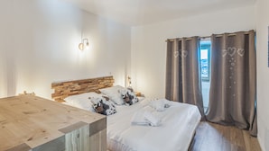 Une chambre avec une tête de lit en bois, un lit avec une literie blanche et des coussins à motifs, un bureau en bois et une fenêtre avec des rideaux.