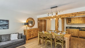 Un salon moderne avec un canapé gris, une table de salle à manger ronde en bois entourée de chaises, une table basse et une lampe.