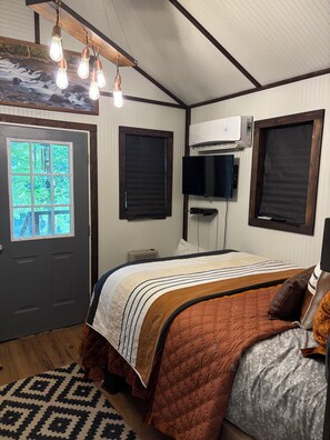 Quarto com cama, televisão, ar-condicionado e janela com persianas.