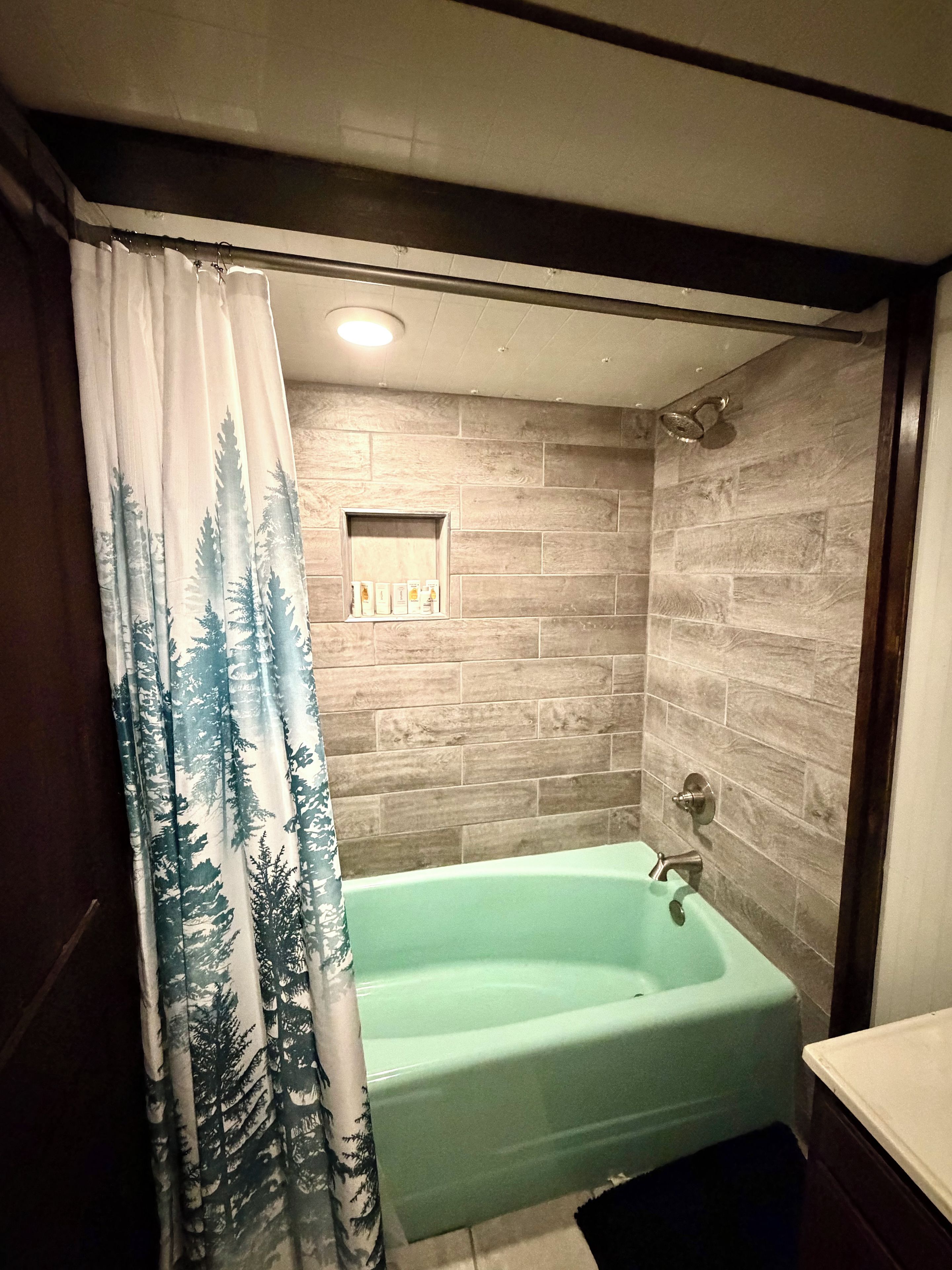 A bathroom with a green bathtub, a shower, and a curtain with a forest pattern.