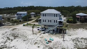 A two-story beachfront house with a balcony and a covered porch.