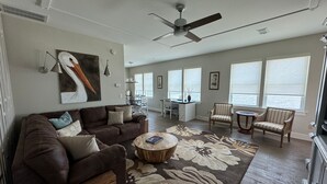 A spacious living room with a brown leather sofa, a round coffee table, and a dining area with white furniture.