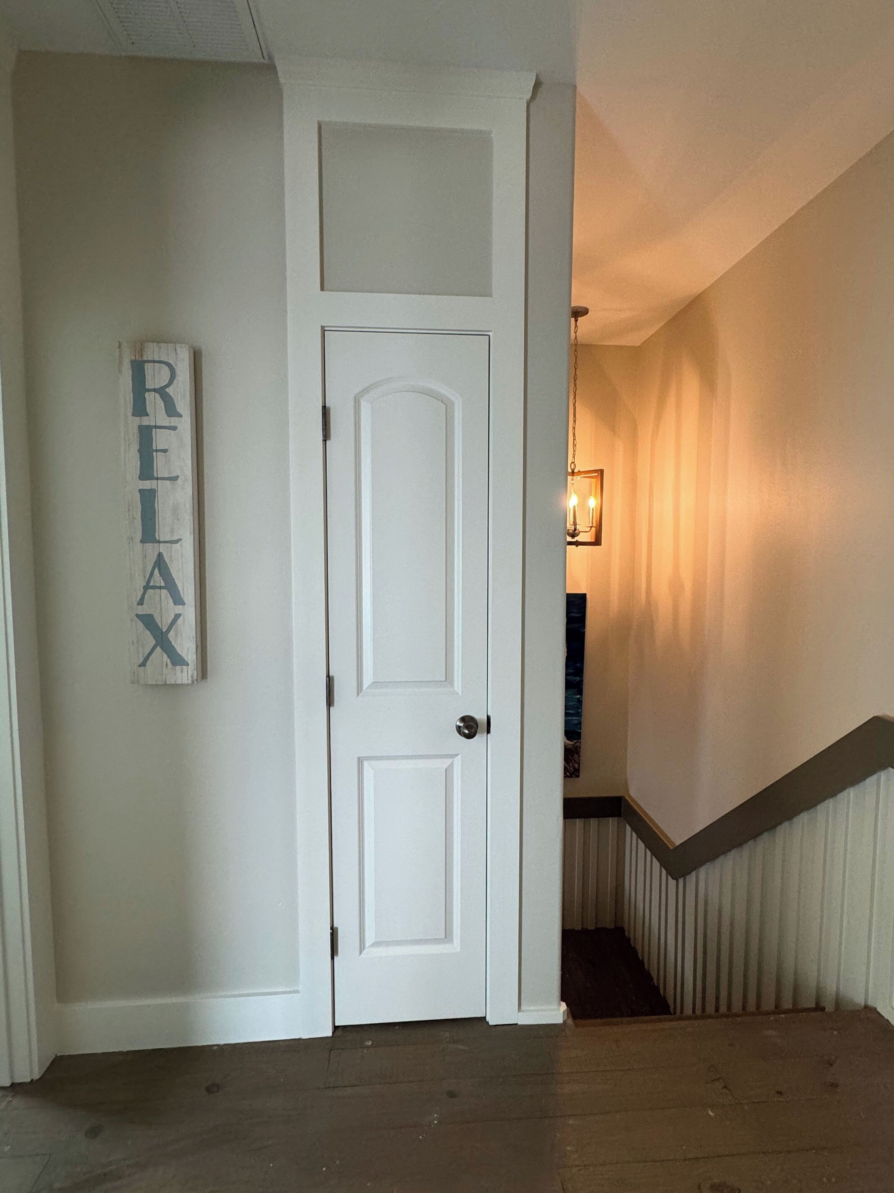 Ein Flur mit einer weißen Tür, einem 'RELAX'-Schild und einer Holztreppe mit Geländer.