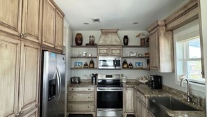 A kitchen with wooden cabinets, stainless steel appliances, a granite countertop, and a window with a view.