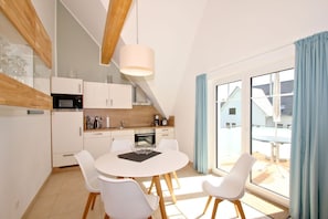 A modern kitchen with white cabinets, a dining table with white chairs, and a large window with blue curtains.
