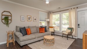 A living room with a grey sofa, round wicker coffee table, wicker chairs, and a white door.