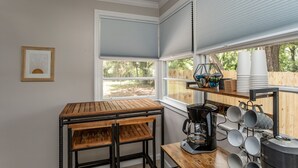 A kitchen with a wooden table and chairs, a coffee maker, and various kitchen utensils on shelves.