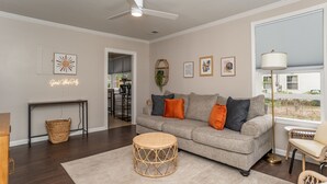 A living room with a grey sofa, round wicker coffee table, and a large window with a view of a house.