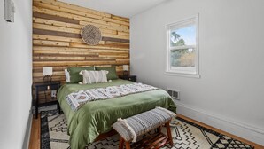 A bedroom with a wooden slat wall, a bed with green bedding, a bench, a window, and a ceiling fan. - The Aztec Casita - Gateway to incredible memories (Forks)