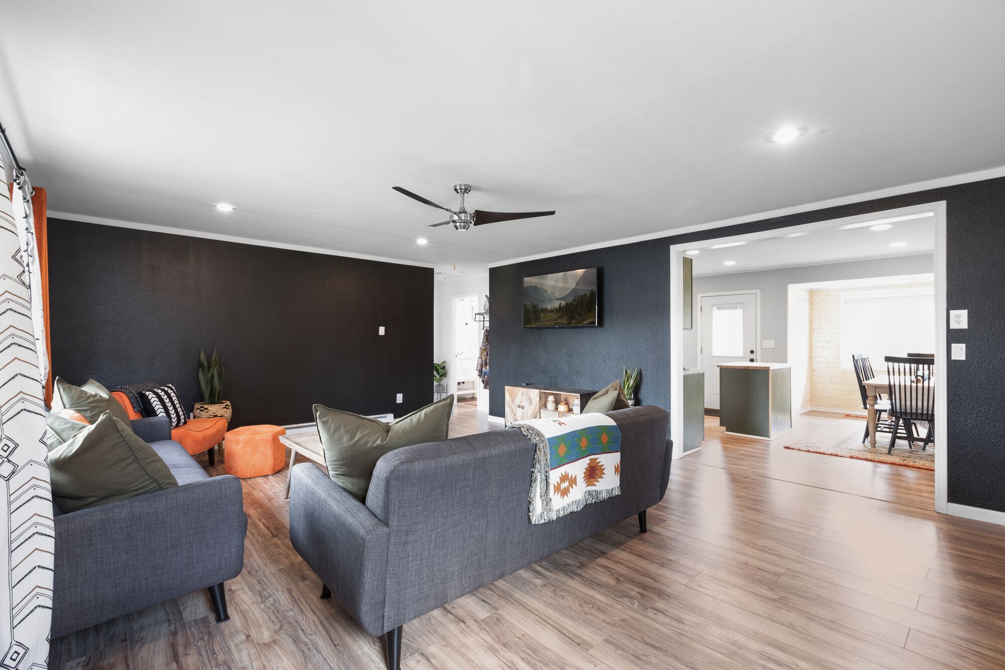 A modern living room with grey sofas, a ceiling fan, and a wooden floor.