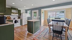 A modern kitchen with green cabinets, a white refrigerator, and a dining area with a wooden table and chairs. - The Aztec Casita - Gateway to incredible memories (Forks)