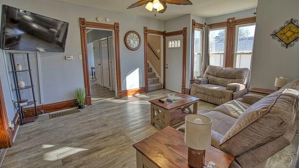 A spacious living room with a wooden floor, a ceiling fan, a sofa, a coffee table, and a TV mounted on the wall. - Great Rural hideaway-20 minutes from peoria (Chillicothe)