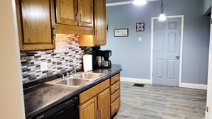 A kitchen with wooden cabinets, a black countertop, and a dishwasher. There is a coffee maker on the counter and a wall-mounted light fixture above. - Great Rural hideaway-20 minutes from peoria (Chillicothe)