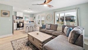 A spacious living room with a large sofa, a coffee table, and a kitchen area in the background. - Canalfront Home with Huge Deck, Close to the Beach (Galveston)
