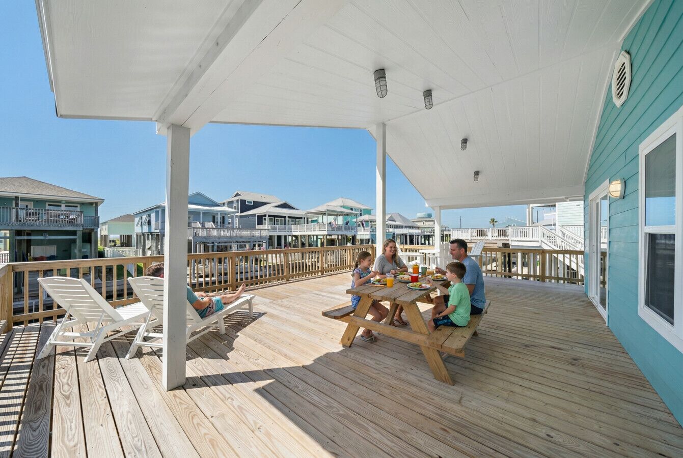 A covered outdoor deck with a wooden picnic table and lounge chairs.