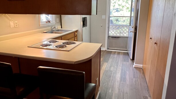 A kitchen with a central island, a sink, and a refrigerator. There is a chair in the foreground and a door leading to a balcony. - Hidden Gem 10 mins to Downtown or Wrightsville Beach. Brand New King Sized Bed (Wilmington)