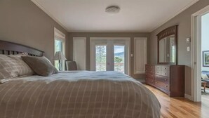 A bedroom with a large bed, a dresser, and a view of the outdoors.