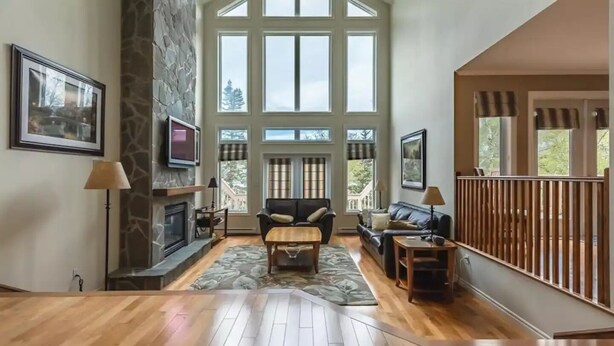 A spacious living room with a fireplace, large windows, and a wooden floor.