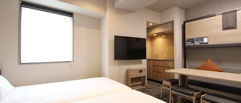 Een hotelkamer met een groot bed, een bureau met stoel, een televisie en een kleine kitchenette.