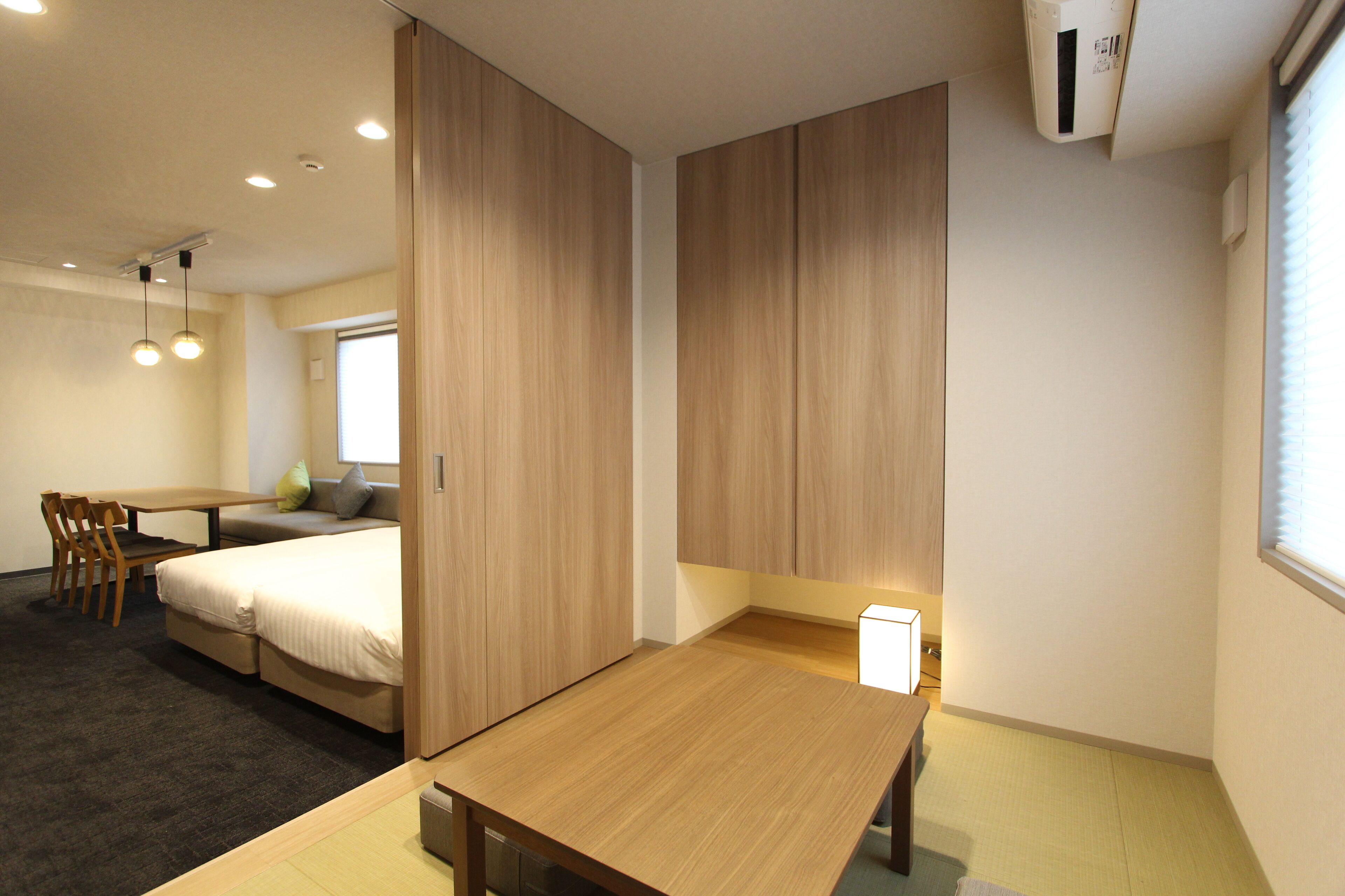 Una habitación de hotel moderna con una cama de madera, un escritorio y una silla. Hay una ventana con persianas y una lámpara en el techo.