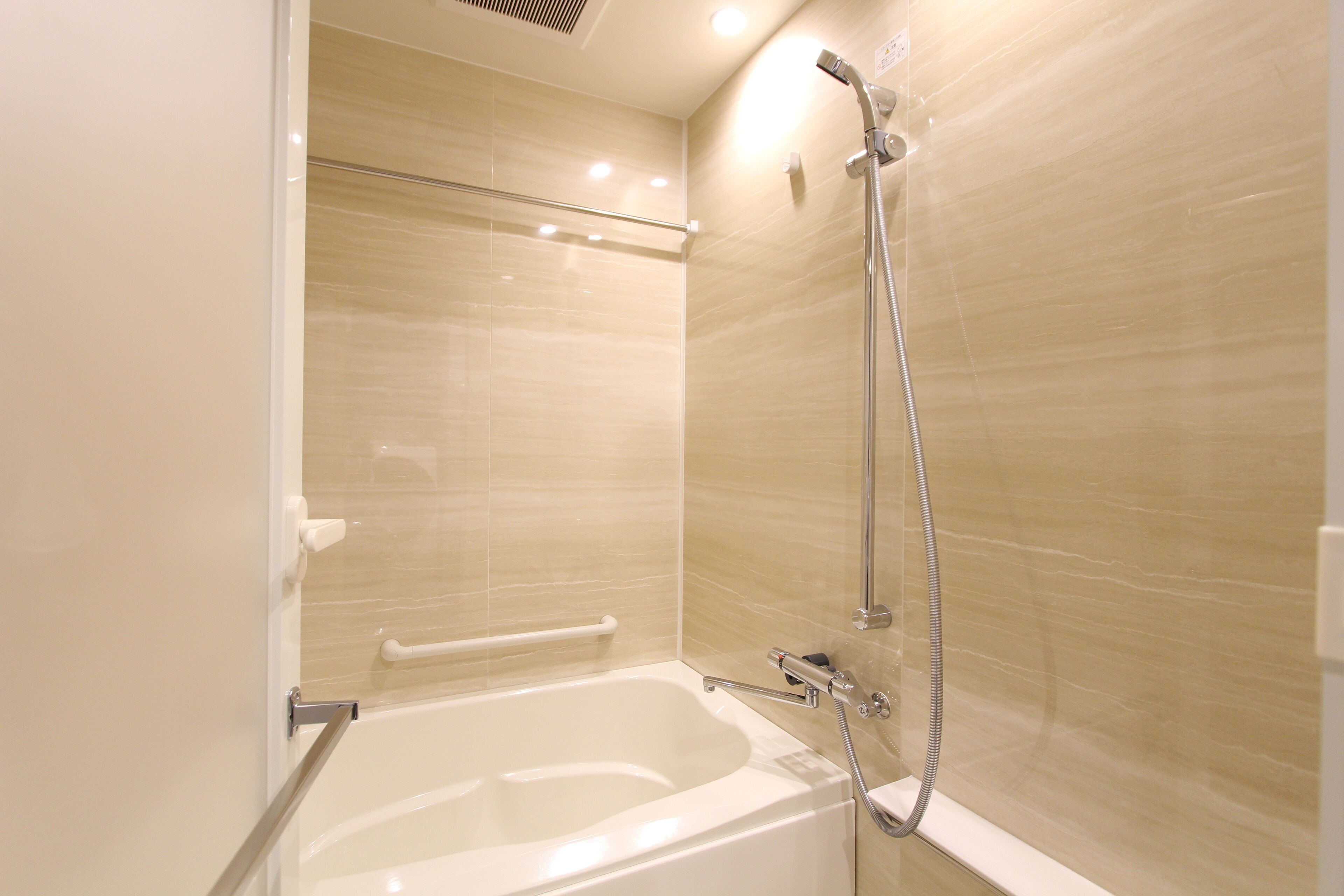 A modern bathroom with a bathtub, shower, and handrails.