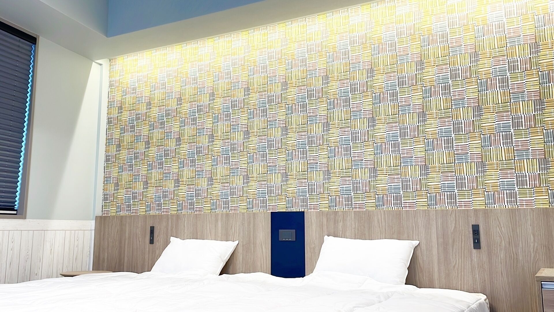 Hotellihuone, jossa on suuri sänky, puinen pääty ja kuvioitu seinä.