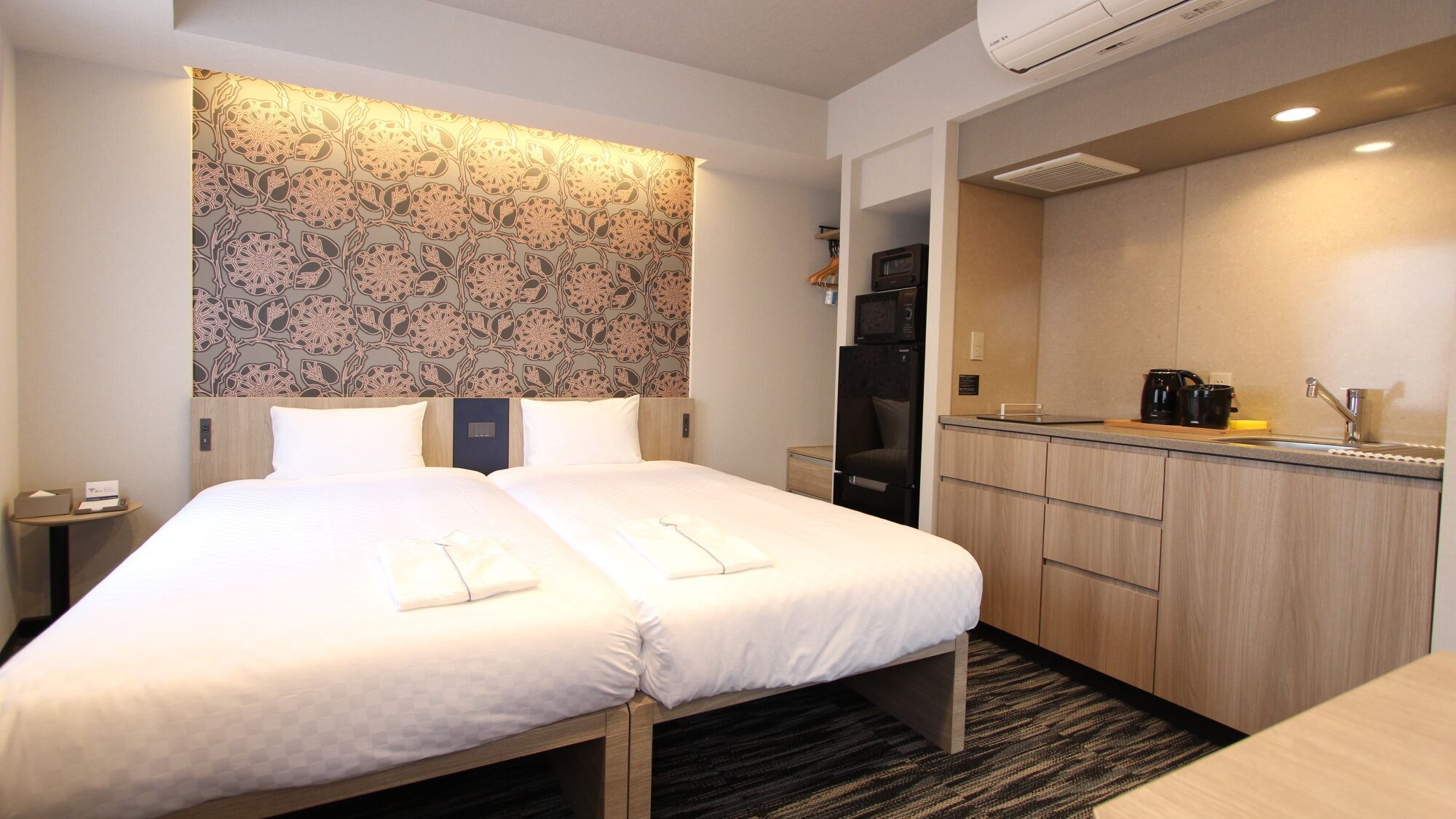 Quarto de hotel com uma cama, uma pequena escrivaninha, um espaço de cozinha e um banheiro.