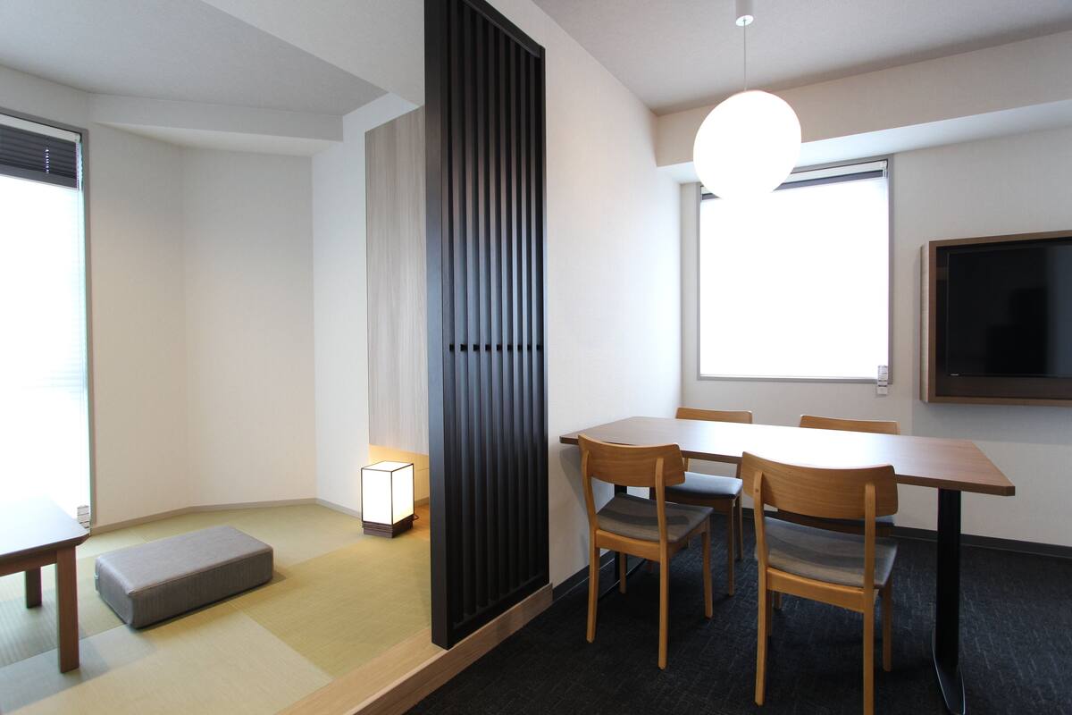 Ein modernes Zimmer mit Tatami-Matten, einem niedrigen Tisch, einer Couch, einem Schreibtisch und Stühlen.