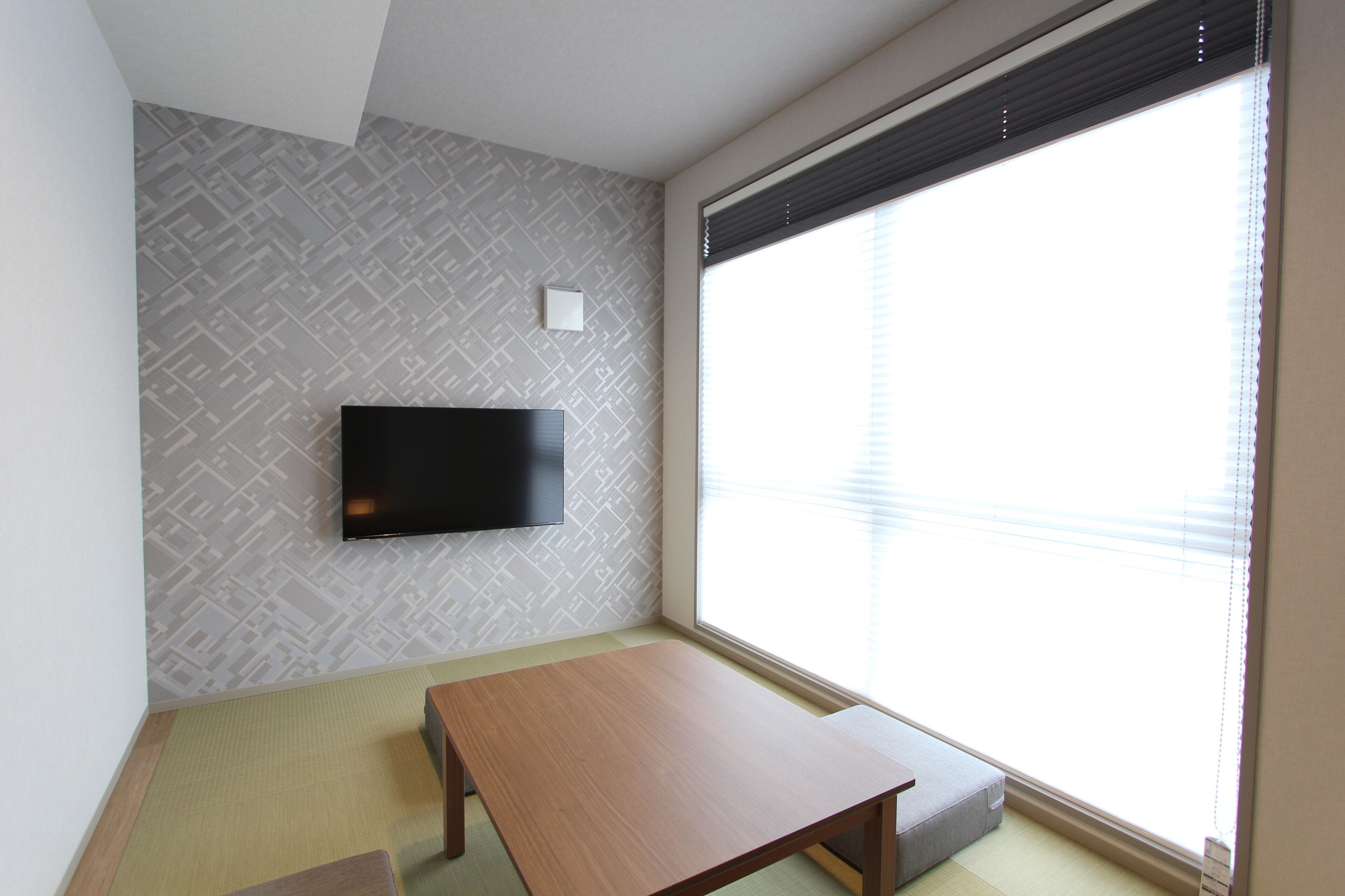 A room with a large window, a flat-screen TV mounted on the wall, and a wooden table.