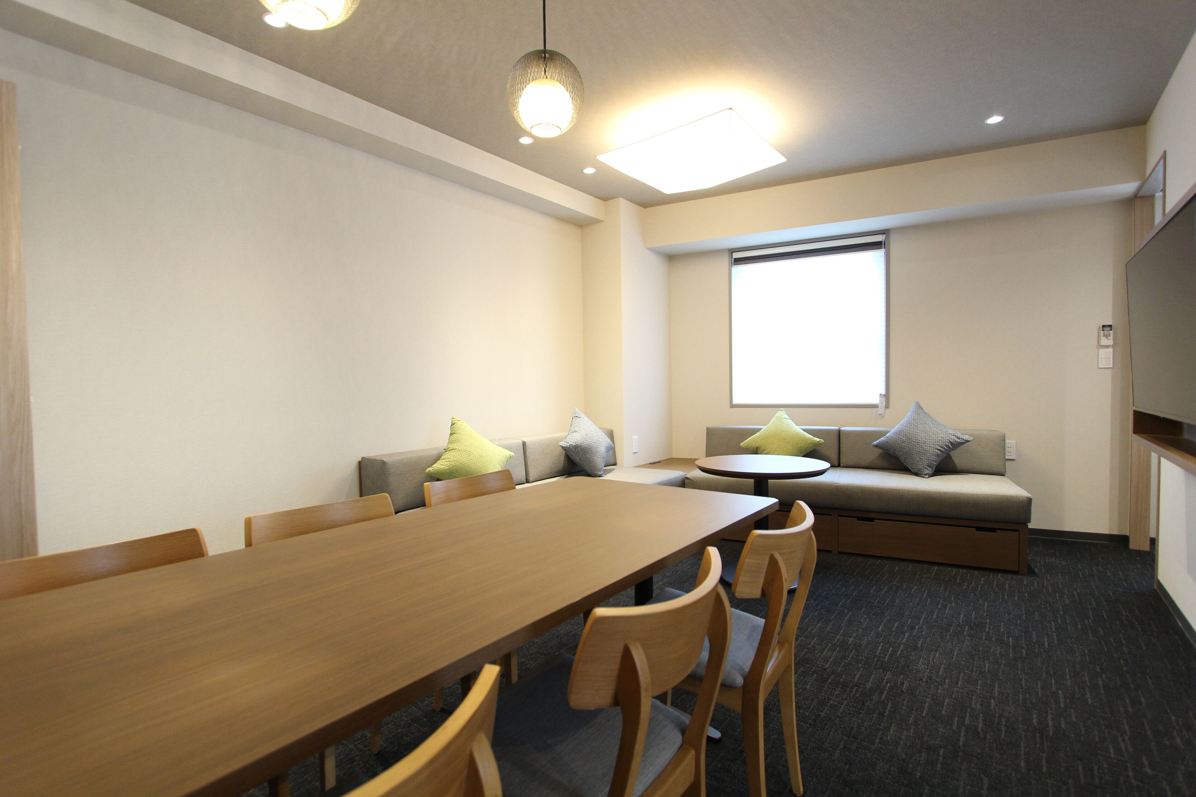 Una sala de conferencias con una larga mesa de madera, varias sillas, un sofá con cojines y un amplio ventanal.