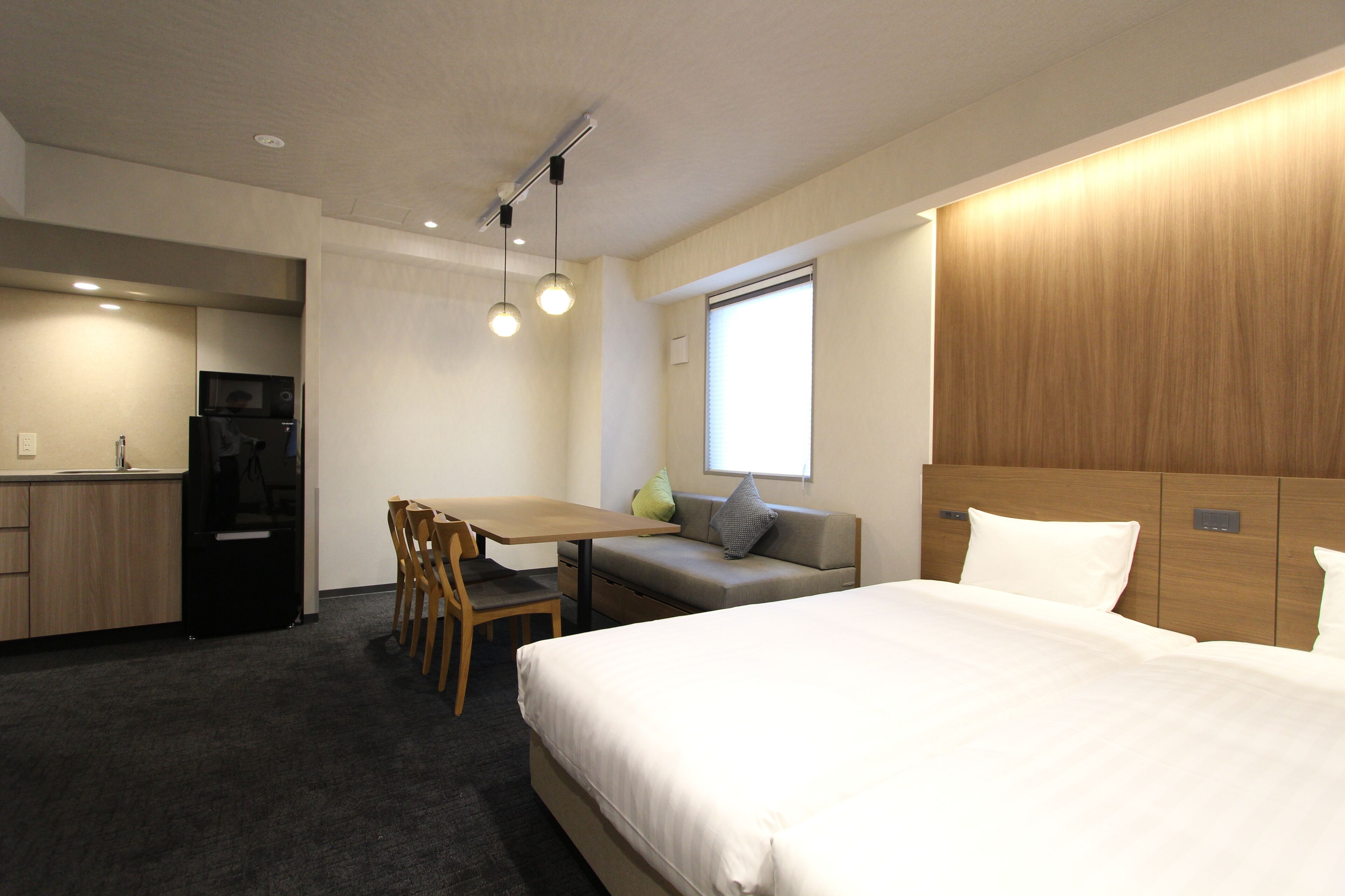 A hotel room with a bed, a sofa, a dining table, and a kitchen area.