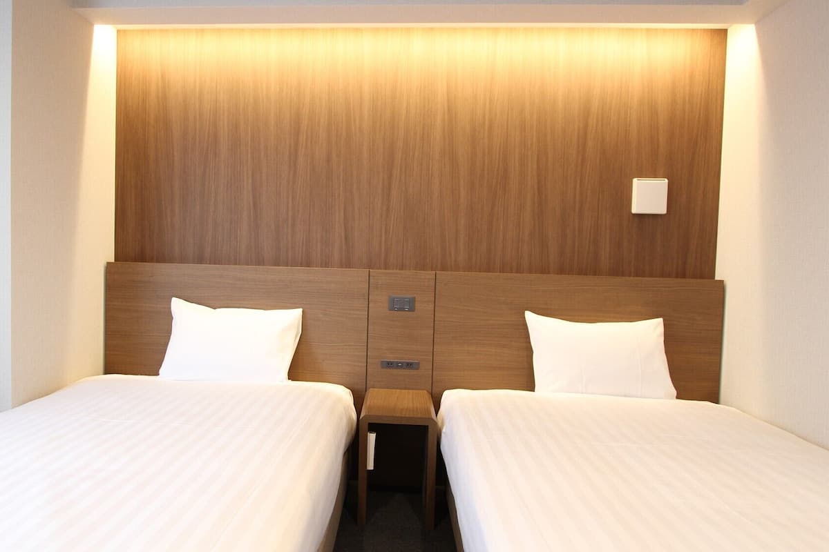 Une chambre d’hôtel avec deux lits, une tête de lit en bois et une table de chevet avec une lampe.