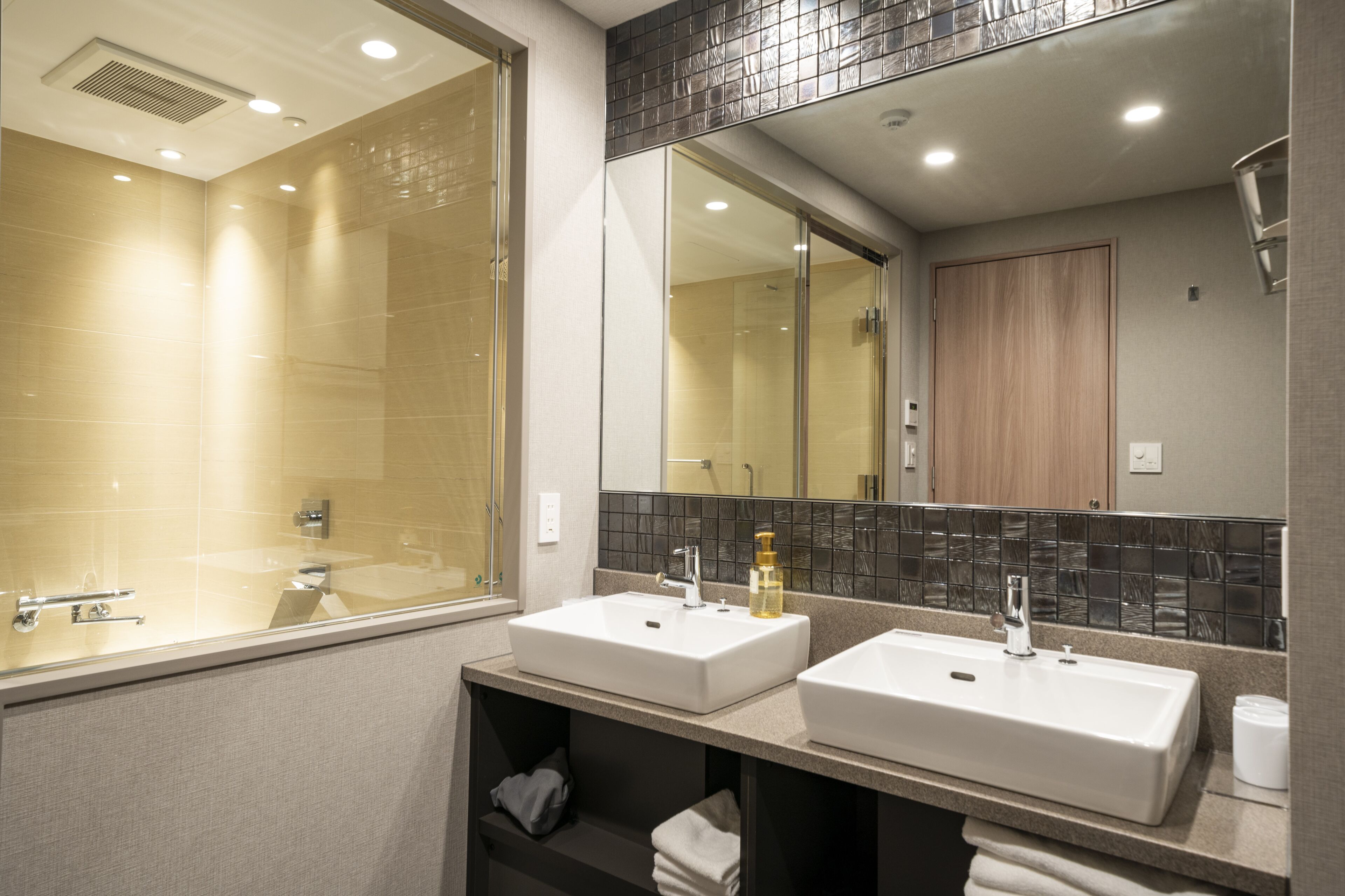 A modern bathroom with two sinks, a large mirror, and a shower area.
