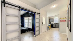A hallway with a sliding door leading to a room with a bed and a window. There is a kitchen area visible in the background. - Single Level 5 Bedrm/Pool/SPA/3Miles Disney (Kissimmee)