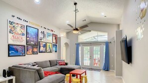 A living room with a grey sectional sofa, a red coffee table, and yellow stools. There are framed Disney movie posters on the wall. - Single Level 5 Bedrm/Pool/SPA/3Miles Disney (Kissimmee)