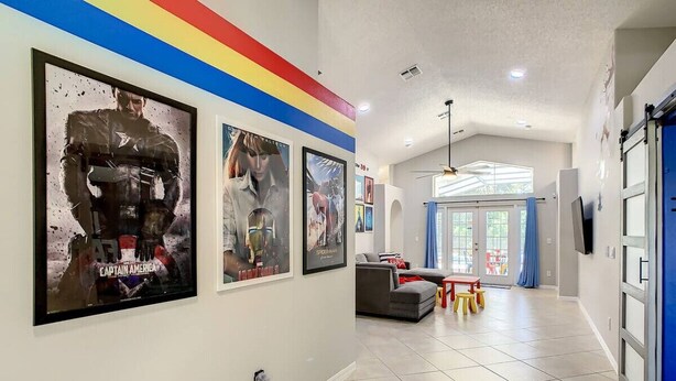 A hallway with framed movie posters, a grey sofa, a small table with stools, and a blue door. - Single Level 5 Bedrm/Pool/SPA/3Miles Disney (Kissimmee)