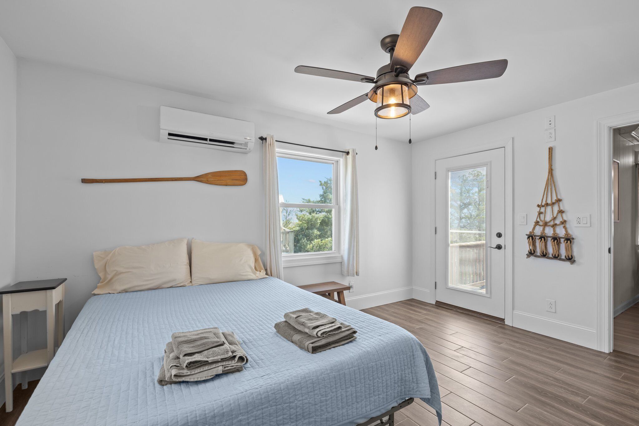 A bedroom with a bed, a ceiling fan, an air conditioning unit, a window, and a door.