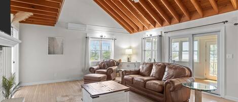 A spacious living room with a high ceiling, leather sofas, a glass coffee table, and a ceiling fan.