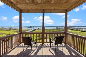 Une terrasse en bois avec deux fauteuils en osier donnant sur le bord de l’eau, avec vue sur un quai et des espaces verdoyants.